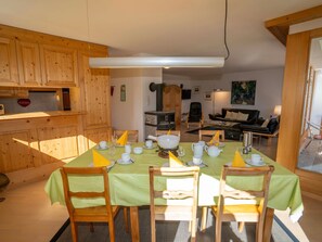 A dining area with a table set for four, wooden chairs, and a kitchen area with wooden cabinets and a stove. - ENZ, (Scuol) by Interhome (Scuol)