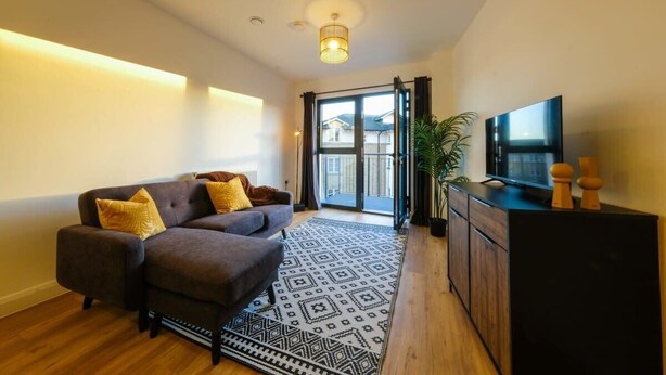 A modern living room with a sofa, a TV, a patterned rug, and a sliding glass door leading to an outdoor area. - Hotwells apartments flat 6- Hopewell (Bristol)