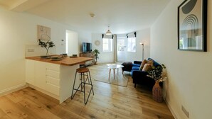 A modern kitchen with a bar area, a dining table, and a sofa in a bright living area with wooden flooring. - Grange Road Two Bedroom Flat (Bristol)