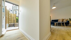 A hallway with a wooden floor, a glass door leading outside, and a dark-colored sofa with cushions. - Grange Road Two Bedroom Flat (Bristol)