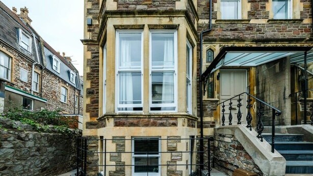 A stone building with a bay window, a staircase, and a stone wall. - Grange Road Two Bedroom Flat (Bristol)