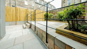 A courtyard with a wooden fence, a staircase, and a garden area with plants. - Grange Road Two Bedroom Flat (Bristol)