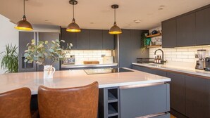 A modern kitchen with dark cabinets, a central island, pendant lighting, and a dining area with chairs. - The Robinson Building (Bristol City)