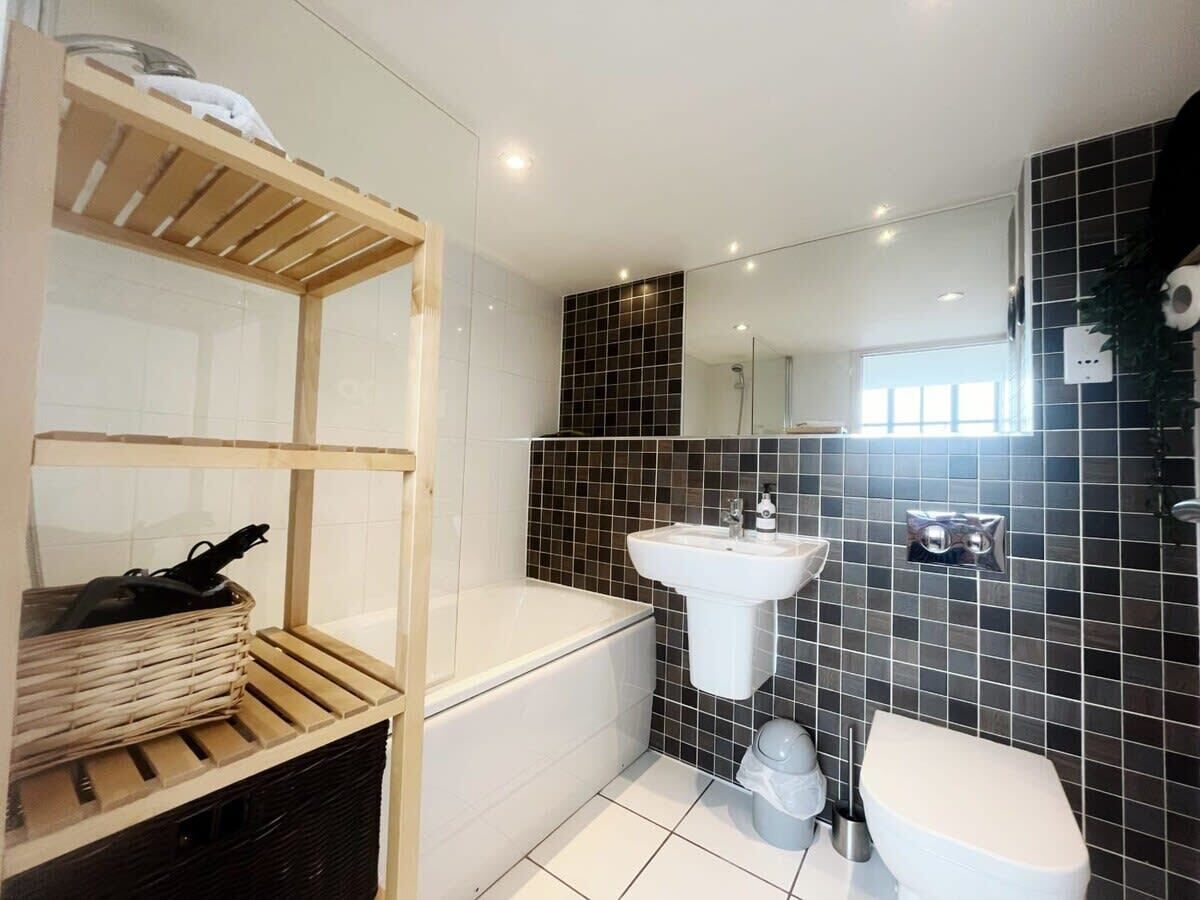 Een badkamer met een badkuip, wastafel, toilet en een plankje met een mandje.