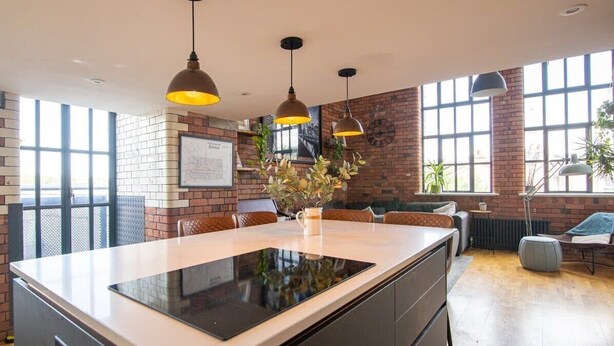 A modern kitchen with a central island, pendant lighting, and a brick wall. - The Robinson Building (Bristol City)
