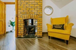 Une pièce avec une cheminée en briques, un fauteuil jaune avec un coussin et un plancher en bois.