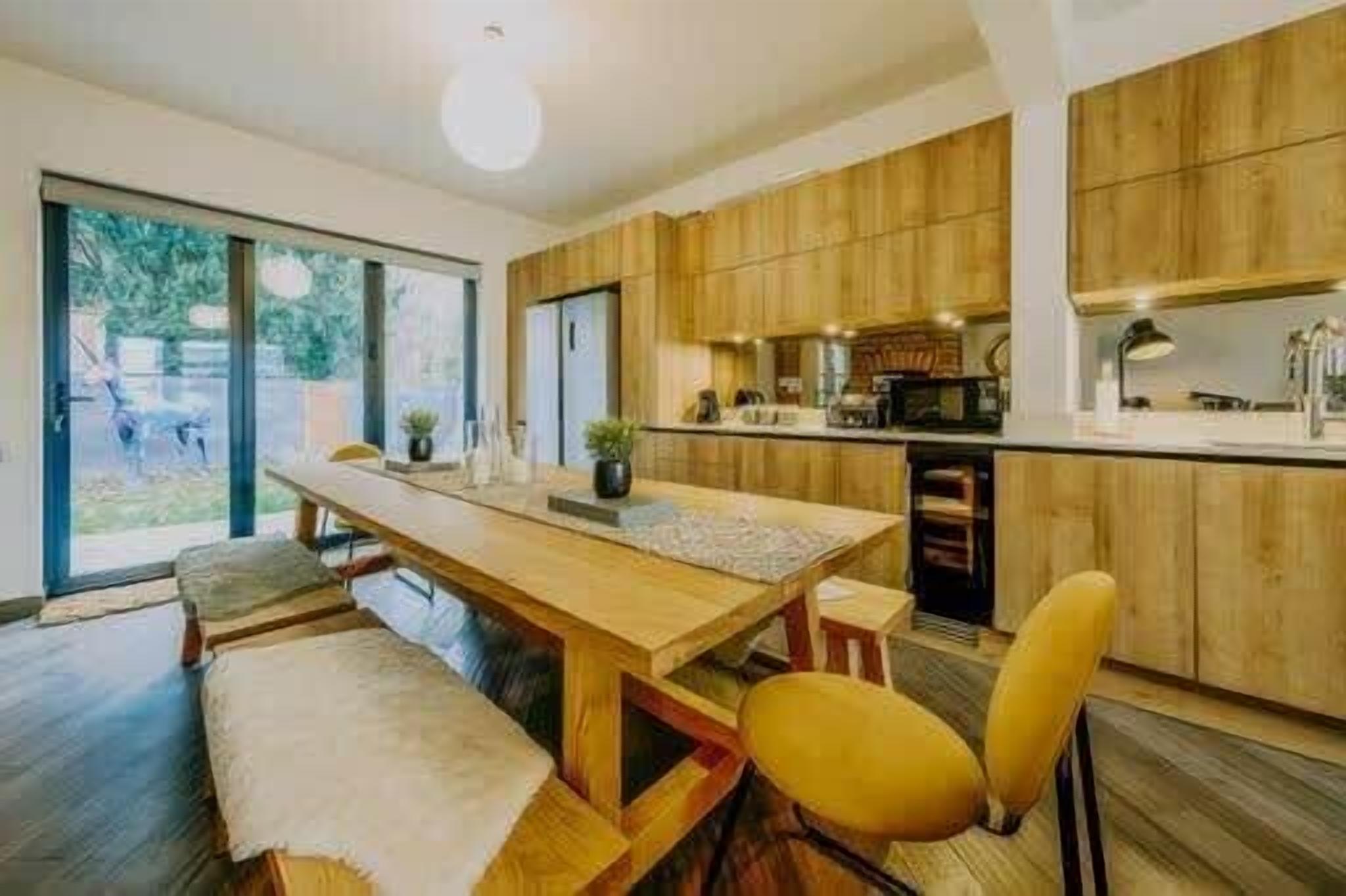A modern kitchen with wooden cabinets, a central island, and a dining area with a bench and chairs.