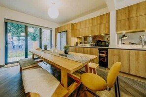 A modern kitchen with wooden cabinets, a central island, and a dining area with a bench and chairs. - Spacious Unicorn House, All Events Welcome! (Bristol City)