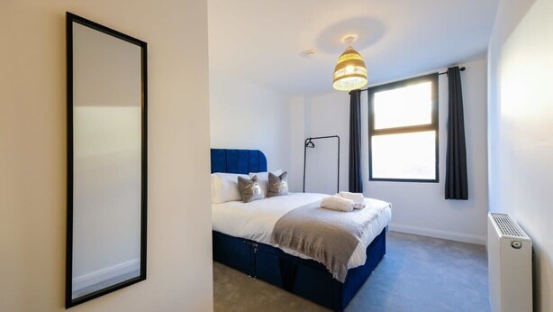 Une chambre à coucher avec un lit, une lampe sur pied, une fenêtre avec des rideaux et un radiateur.