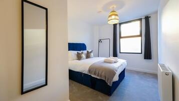 A bedroom with a bed, a standing lamp, a window with curtains, and a radiator.