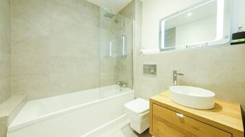 A modern bathroom with a glass-enclosed shower, a white bathtub, a toilet, and a wooden vanity with a white sink.