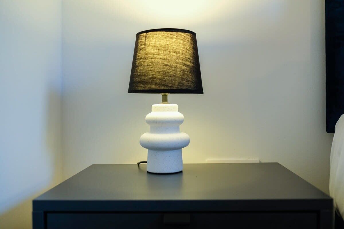 Eine weiße Tischlampe mit schwarzem Lampenschirm auf einem Nachttisch.
