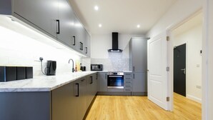 Une cuisine moderne avec des meubles gris, un plan de travail blanc, un four encastré et un four à micro-ondes.