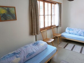Een kamer met twee eenpersoonsbedden, een stoel, een radiator en een raam met gordijnen.