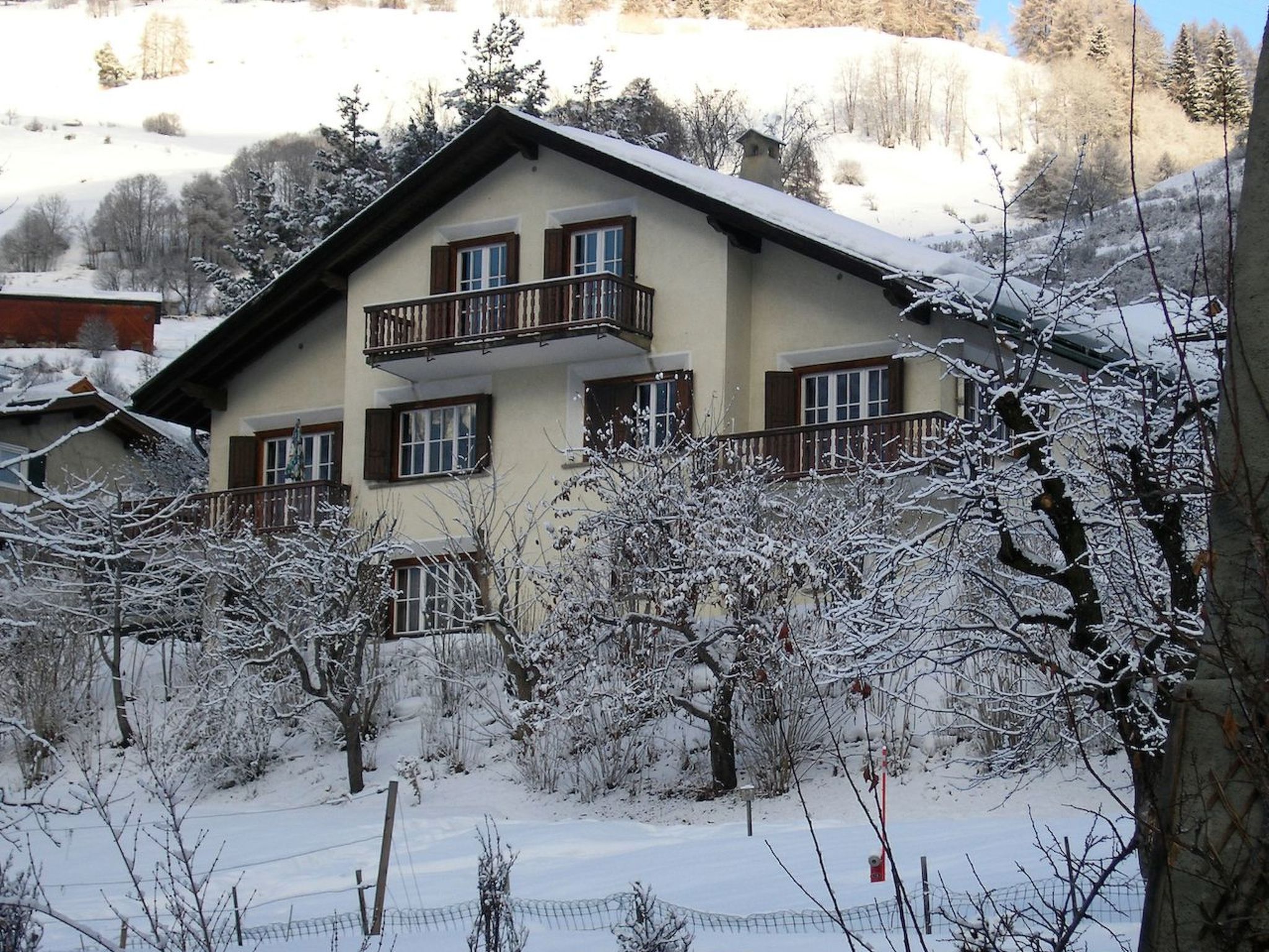 Un immeuble à plusieurs étages doté d’un balcon au deuxième étage, entouré d’arbres couverts de neige et surplombant un ciel dégagé.