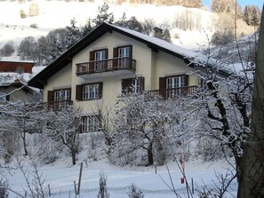 A multi-story building with a balcony on the second floor, surrounded by snow-covered trees and a clear sky. - Ferienhaus Chasa Allegra, (Scuol) by Interhome (Scuol)