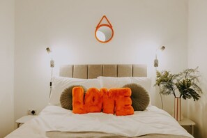 Una cama con cabecera, un espejo fijado a la pared, lámparas de noche y una almohada decorativa que dice 'LOVE'.