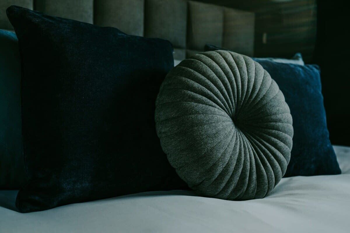 A bed with dark blue pillows and a single grey pillow.