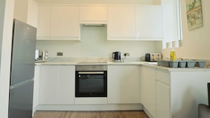 A modern kitchen with white cabinets, a built-in oven, a refrigerator, and a coffee maker. - Winchester two bedroom property in Brislington (Bristol)