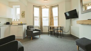 A modern room with a kitchenette, a dining area, a TV, and a large window with curtains. - Winchester two bedroom property in Brislington (Bristol)