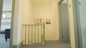 A hallway with a wooden railing, a carpeted floor, and three framed pictures on the wall. - Winchester two bedroom property in Brislington (Bristol)