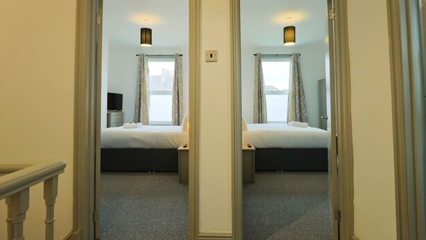 A mirrored hallway leading to a bedroom with a bed, bedside table, and a lamp. - Winchester two bedroom property in Brislington (Bristol)
