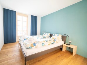 A bedroom with a bed, a bedside table, a lamp, and a window with curtains. - Chasa Muntanella, (Ftan) by Interhome (Ftan)