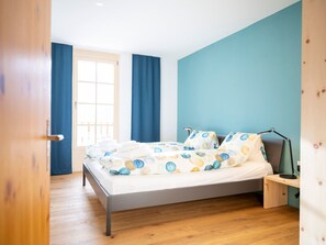 A bedroom with a bed, a nightstand, a desk, and a window with curtains. - Chasa Muntanella, (Ftan) by Interhome (Ftan)