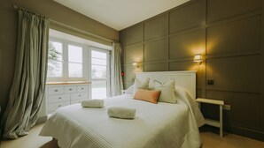 Ein Schlafzimmer mit einem großen Bett, Nachttischen, einem Fenster mit Vorhängen und Wandleuchten.