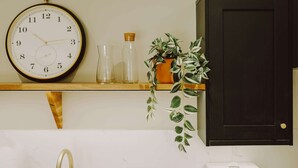 Eine Wanduhr, ein Regal mit Glasflaschen und einem Blumentopf, sowie ein dunkles Schranksystem.