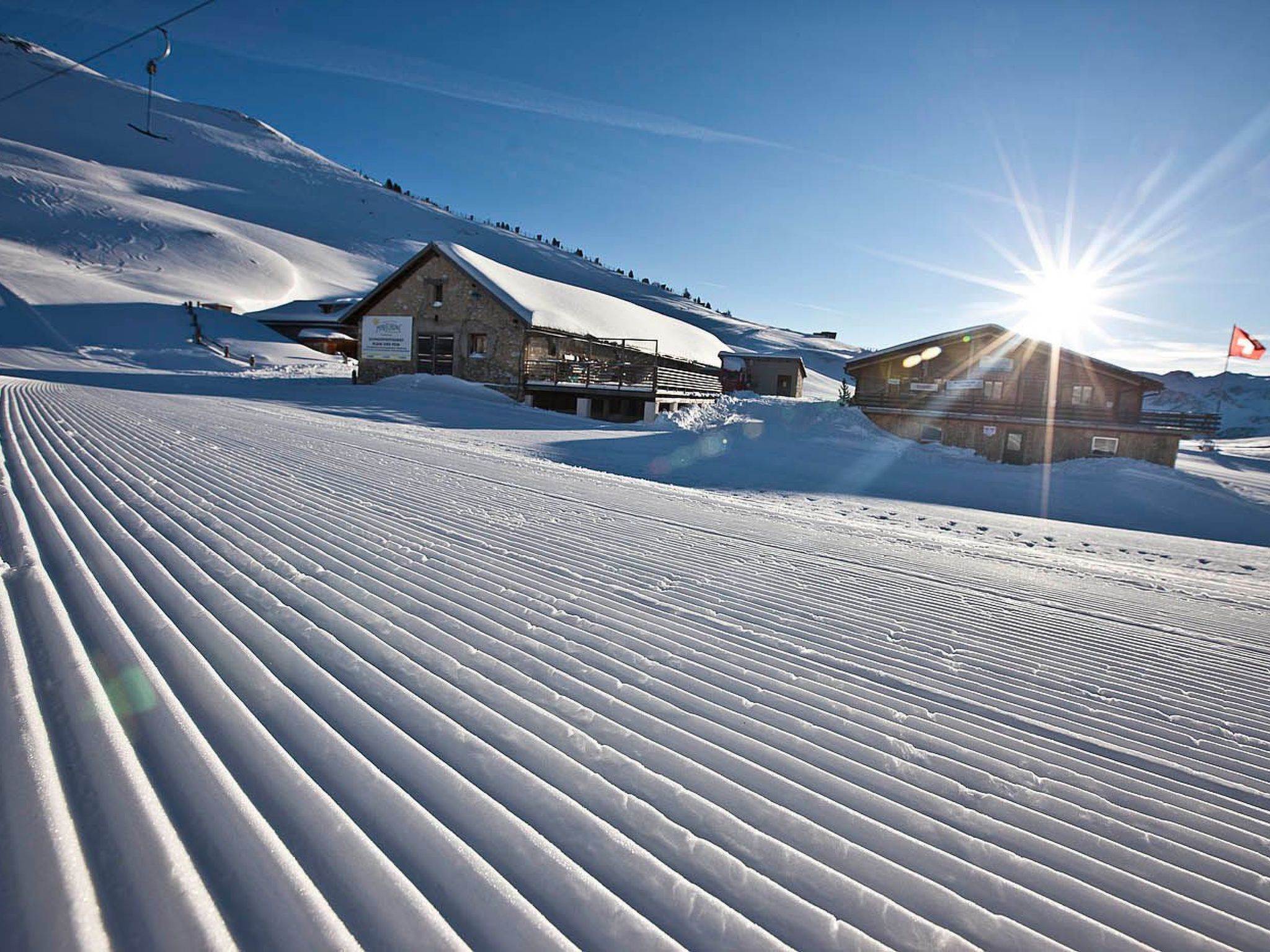 Una pista da sci innevata con un edificio in legno e una seggiovia sullo sfondo.