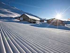 Ein mit Schnee bedeckter Skiabhang mit einem Holzbau und einer Seilbahn im Hintergrund.