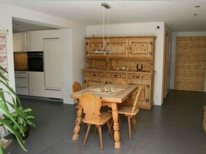 Ein Essbereich mit Holztisch und -stühlen, eine Küche mit weißen Schränken und ein großes Holzregal mit Schubladen.