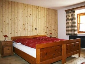 Ein Schlafzimmer mit einem hölzernen Bett, einem Nachttisch, einem Fenster mit Vorhängen und Holzvertäfelung.