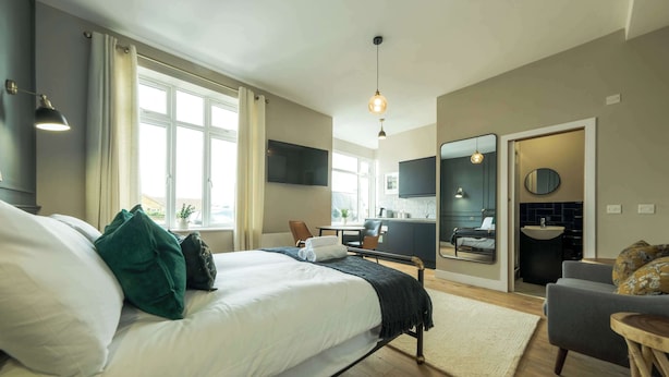 Et moderne hotelværelse med seng, skrivebord, stol, spejl og udsigt over byen.