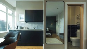 Et moderne køkken med mørke skabe, en hvid bordplade og et spiseområde med en stol.