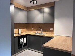 A modern kitchen with grey cabinets, a wooden countertop, and a built-in dishwasher. - 7Mins City Garden and Center+P (Plovdiv)