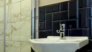 Un baño con un lavamanos blanco, paredes de azulejos negros y una cabina de ducha de vidrio.