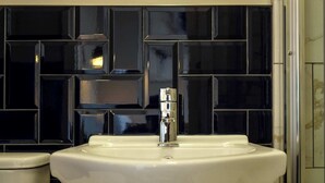 A bathroom with a white sink, a chrome faucet, and black tiled walls.