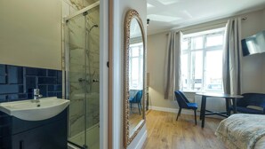 A hotel room with a shower, a sink, a mirror, a bed, a table, and a chair.