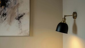 A wall-mounted lamp with a black shade and brass accents, positioned next to a large abstract painting on a plain wall.
