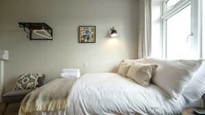 Un dormitorio con una cama, una silla, un perchero en la pared, una lámpara de pared y una ventana.