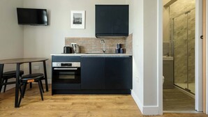 Una cocina compacta con horno empotrado, un mueble negro, un televisor de pantalla plana y una pequeña mesa de comedor con dos sillas.