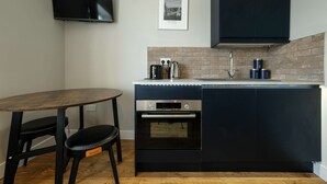 Una cocina compacta con horno integrado, cafetera y un mueble negro.