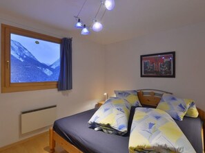 A bedroom with a bed, a window with a mountain view, a framed picture on the wall, and a ceiling light fixture. - TRAFÖGL, (Scuol) by Interhome (Scuol)