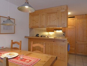 A kitchen with wooden cabinets, a dining table with chairs, and a pendant light. - TRAFÖGL, (Scuol) by Interhome (Scuol)