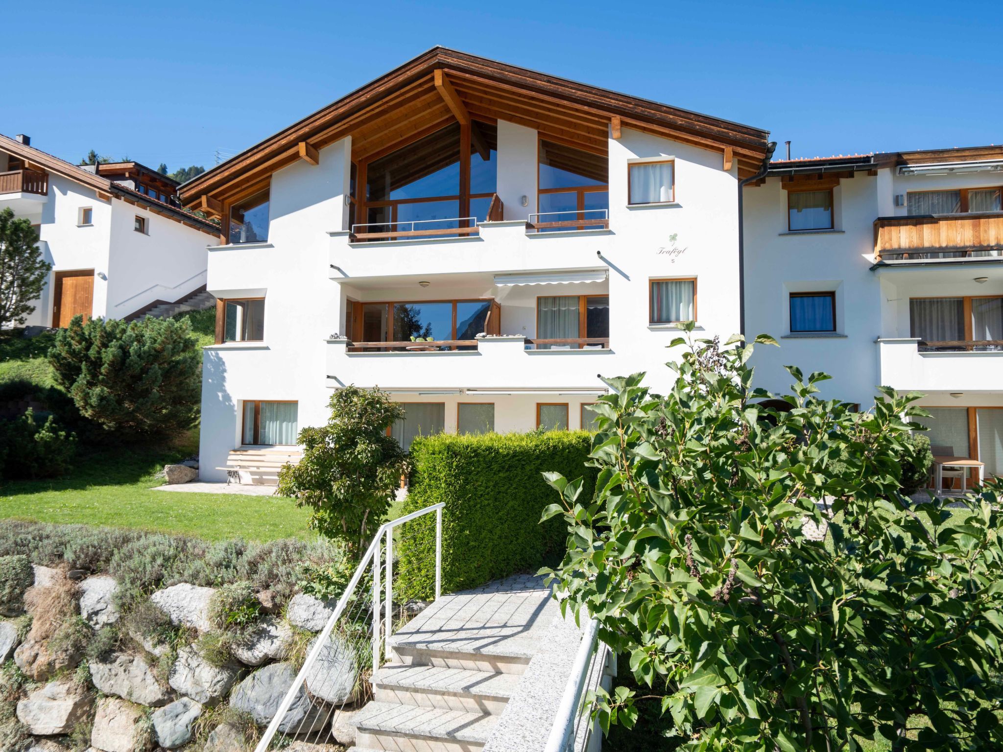A multi-story residential building with a modern design, featuring balconies, large windows, and a well-maintained garden area.