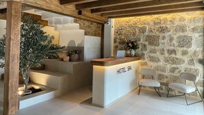 A hotel reception desk with a stone wall backdrop, a staircase, and a small indoor plant.