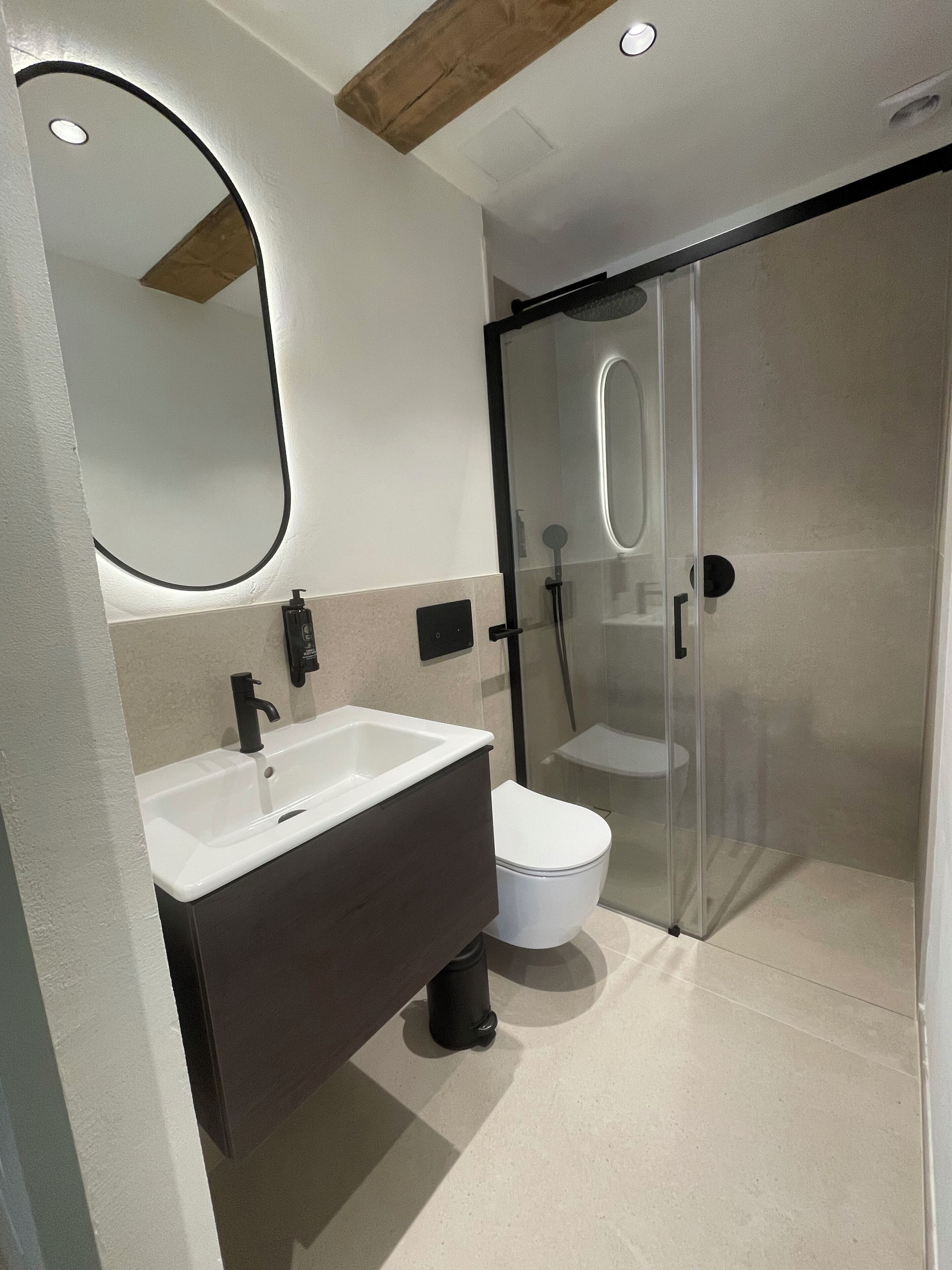 Un baño moderno con un espejo grande, un lavabo, un inodoro y una ducha con cerramiento de vidrio.