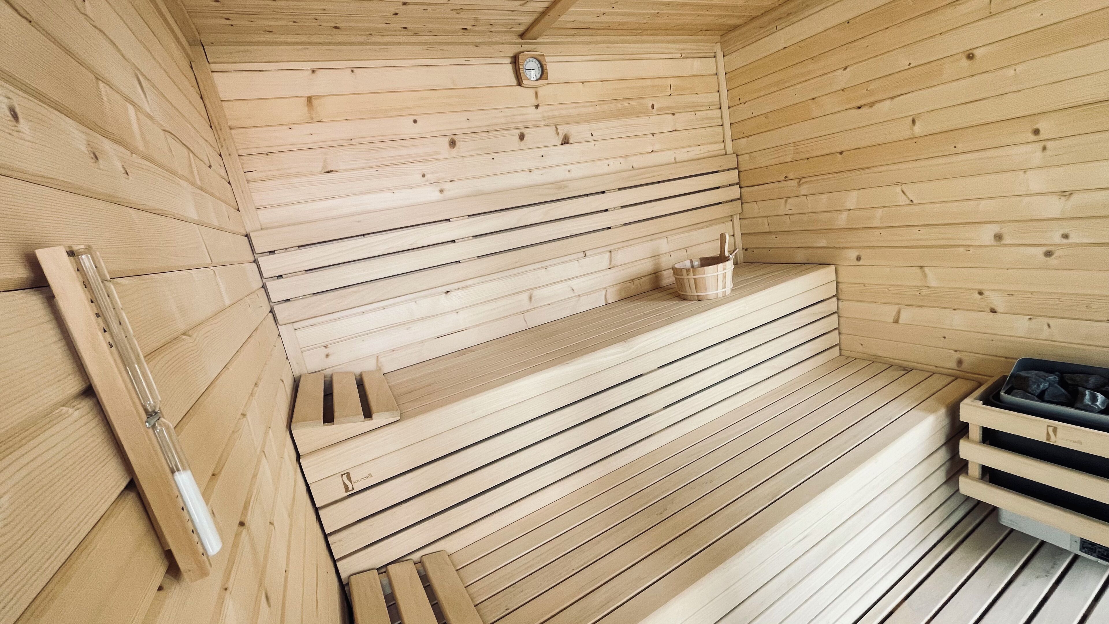 A wooden sauna with benches, a wooden bench, and a small shelf with a clock.